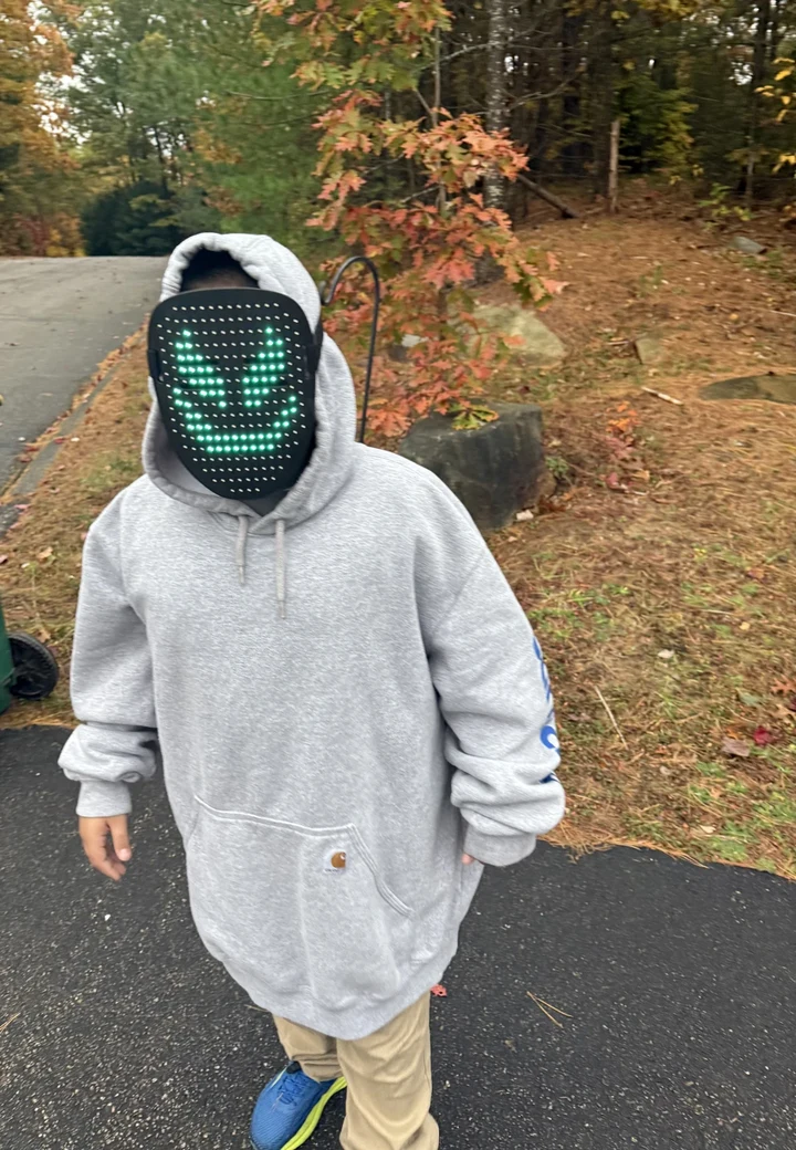 Rocco outdoors in autumn, wearing a gray hoodie and a light-up mask with a green face